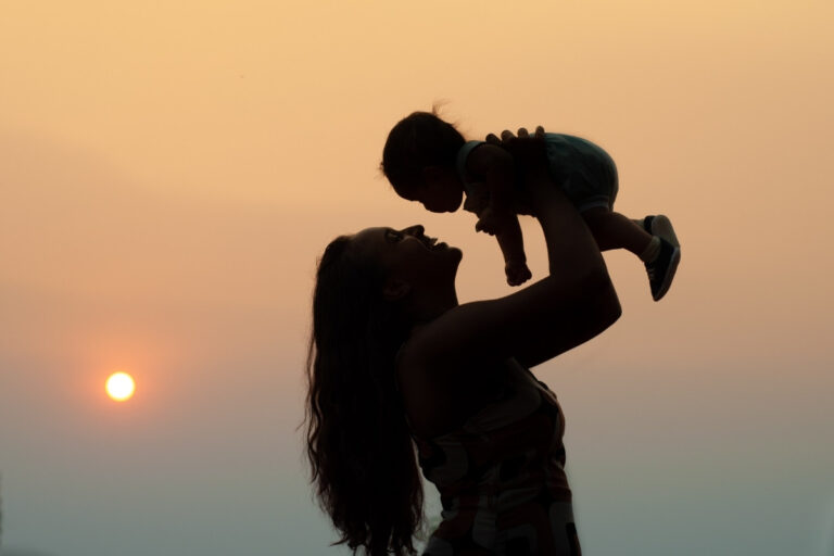 Mãe levantando bebê ao pôr do sol representando versículos para homenagear as mães